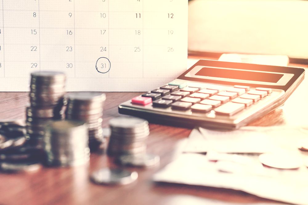 A stack of coins is sitting on a table next to a calculator and a calendar.