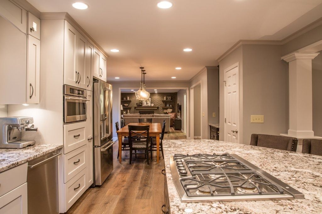 Kitchen with granite island, stove, white cabinets, stainless steel appliances, and wood floor. Dining area in background.
