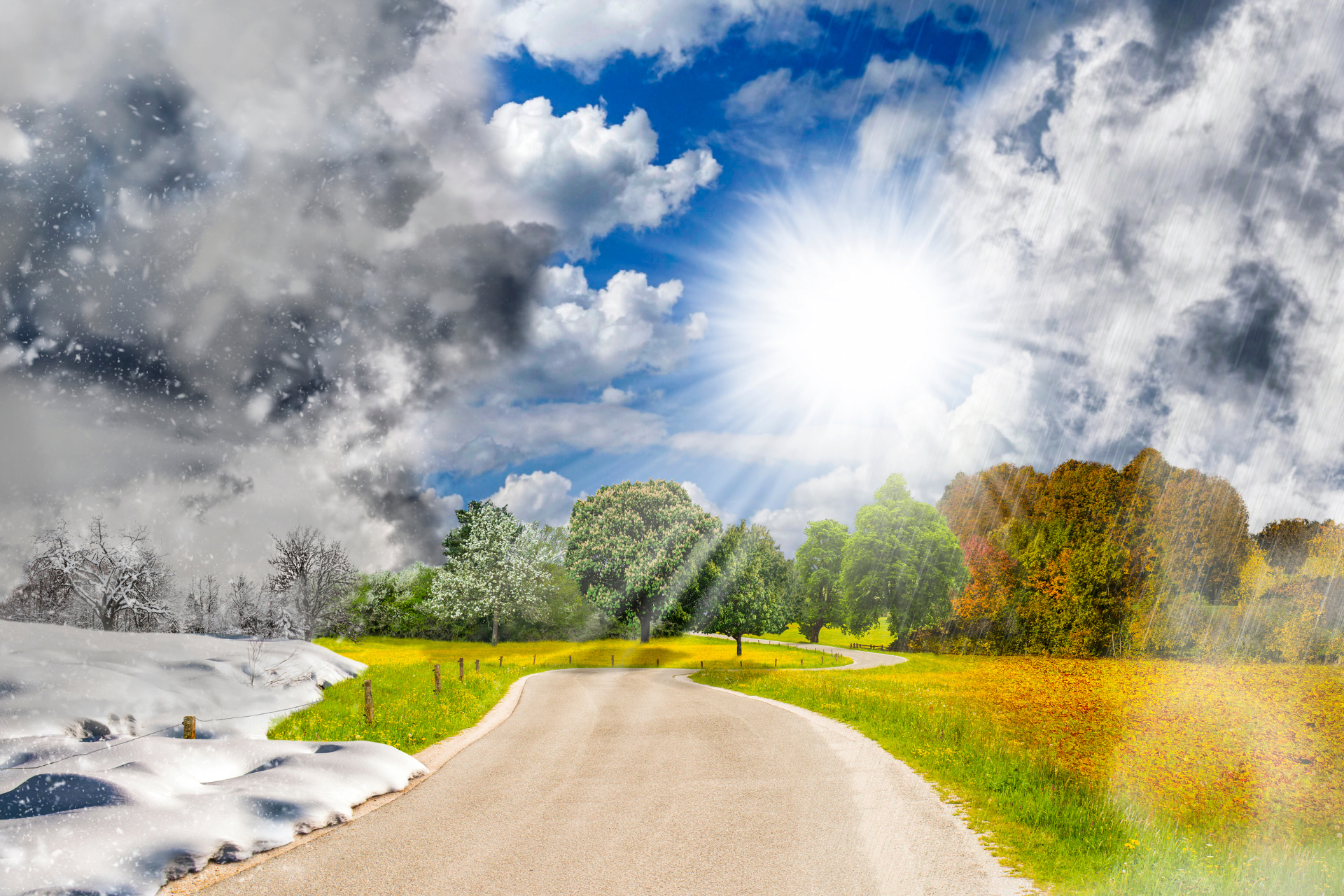 A road going through a field with the sun shining through the clouds.