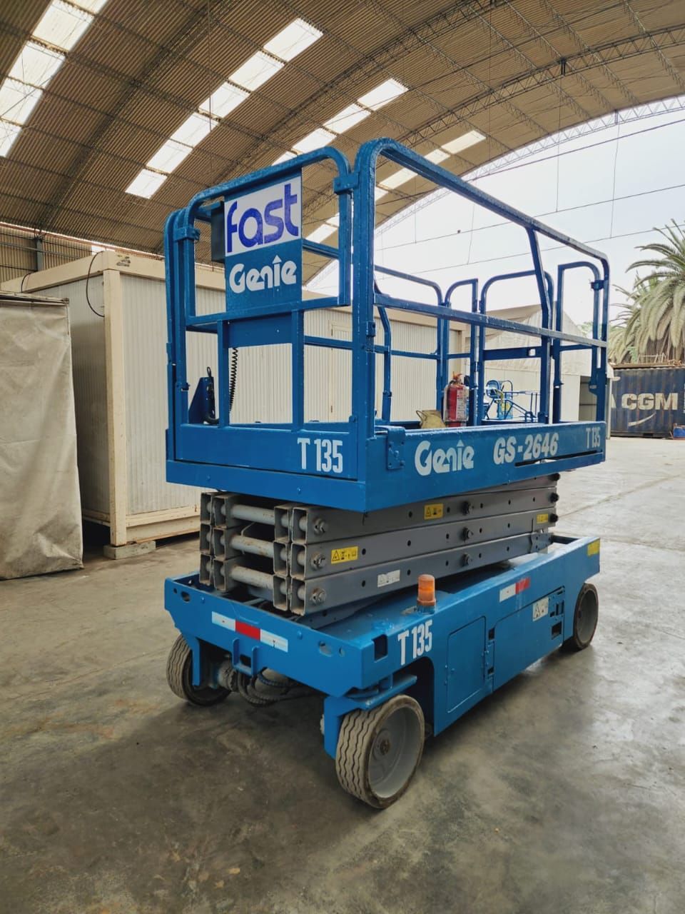 Plataforma elevadora de tijera Blue Genie T30 estacionada en el interior de un almacén con una marquesina blanca sobre la plataforma.