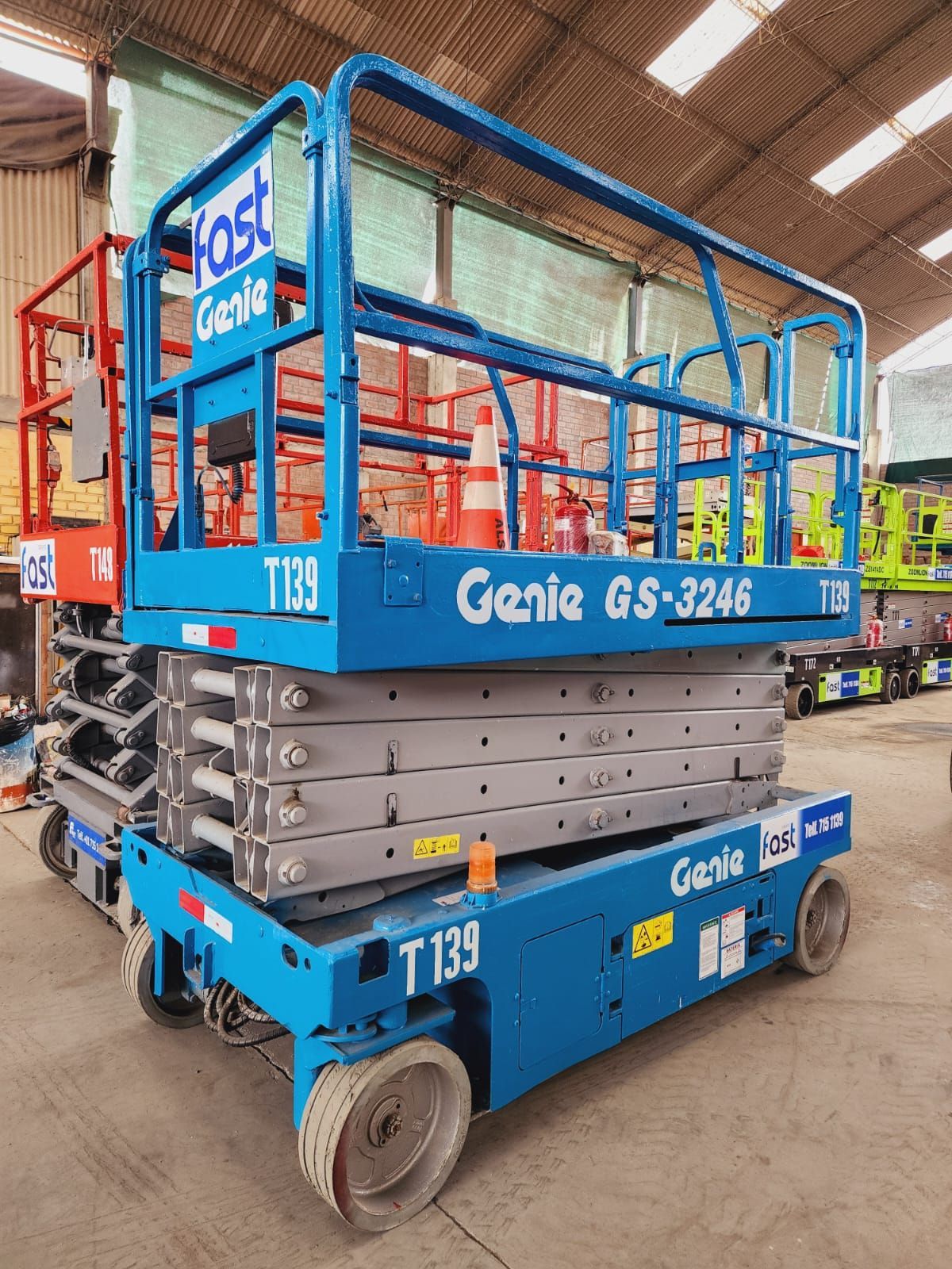 Plataforma elevadora de tijera Blue Genie GS-3246 con barandilla de seguridad roja en un almacén industrial.