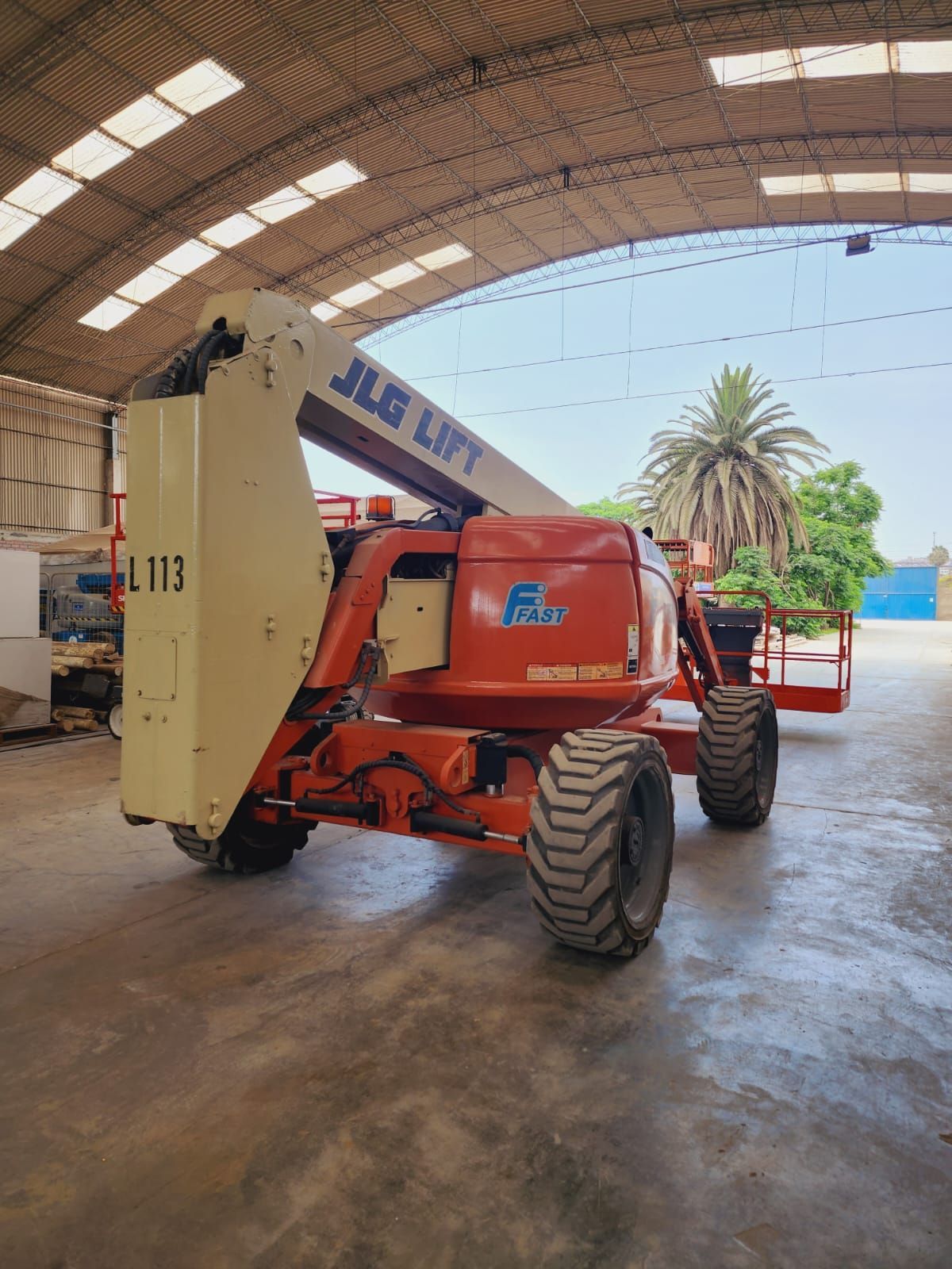 Carretilla elevadora JLG naranja aparcada dentro de un almacén con techo alto arqueado.