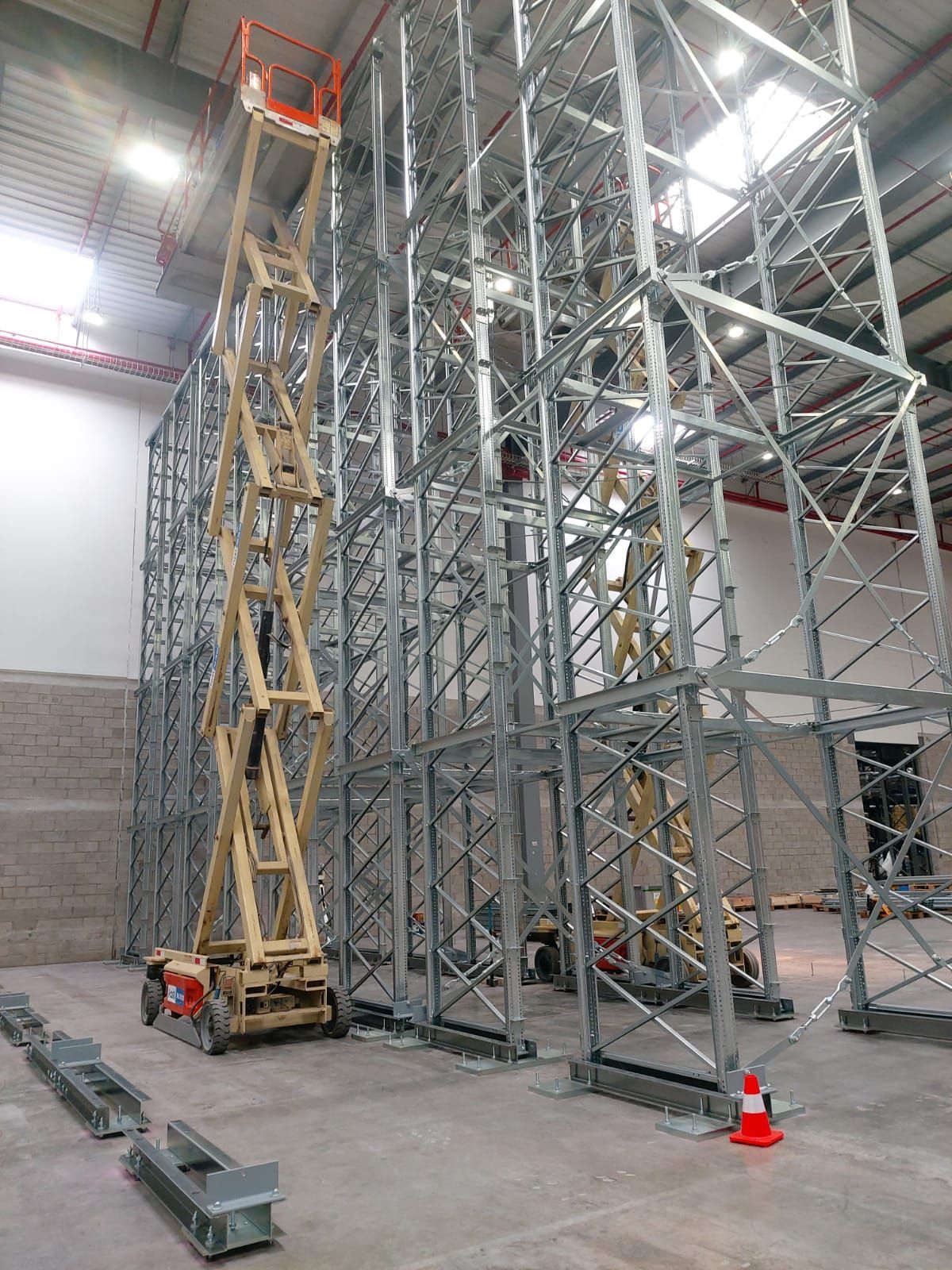 Andamio industrial alto con una plataforma elevadora de tijera amarilla dentro de un almacén en construcción.