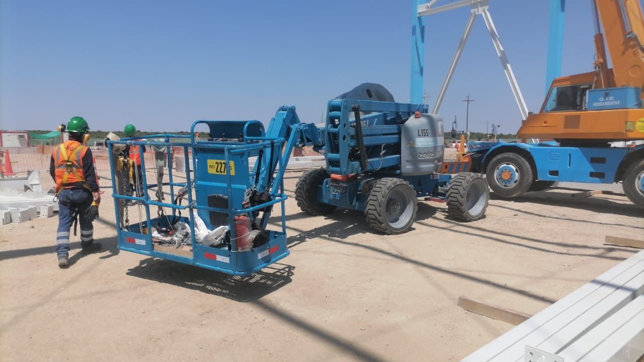 Obreros de la construcción y plataformas elevadoras azules en un soleado emplazamiento industrial cerca de una grúa.