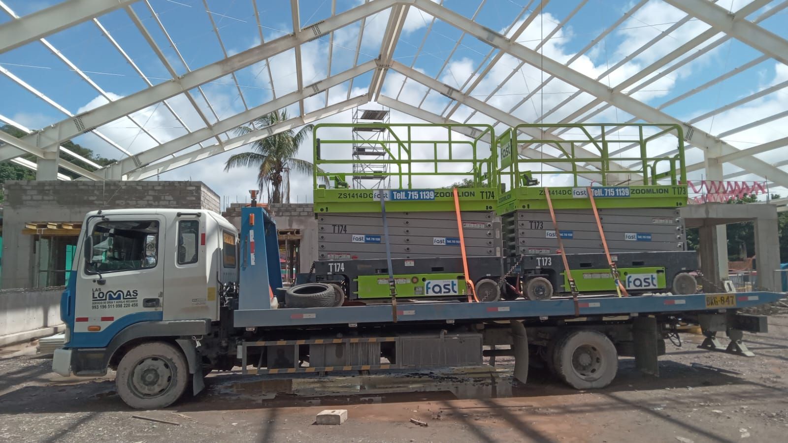 Camión de plataforma que transporta estructuras metálicas bajo una estructura con techo de vidrio.