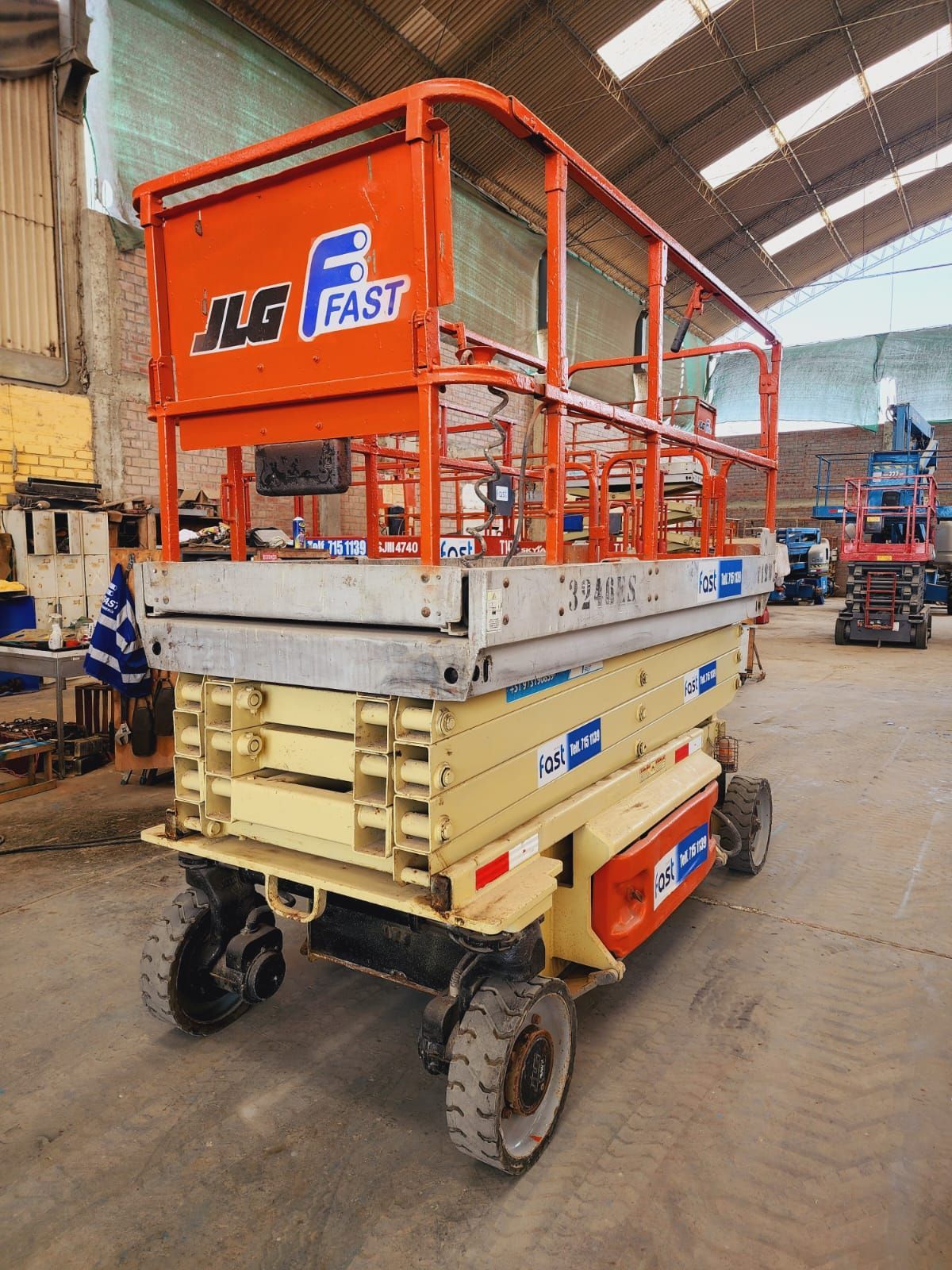 Plataforma elevadora de tijera JLG naranja estacionada dentro de un taller de almacén.