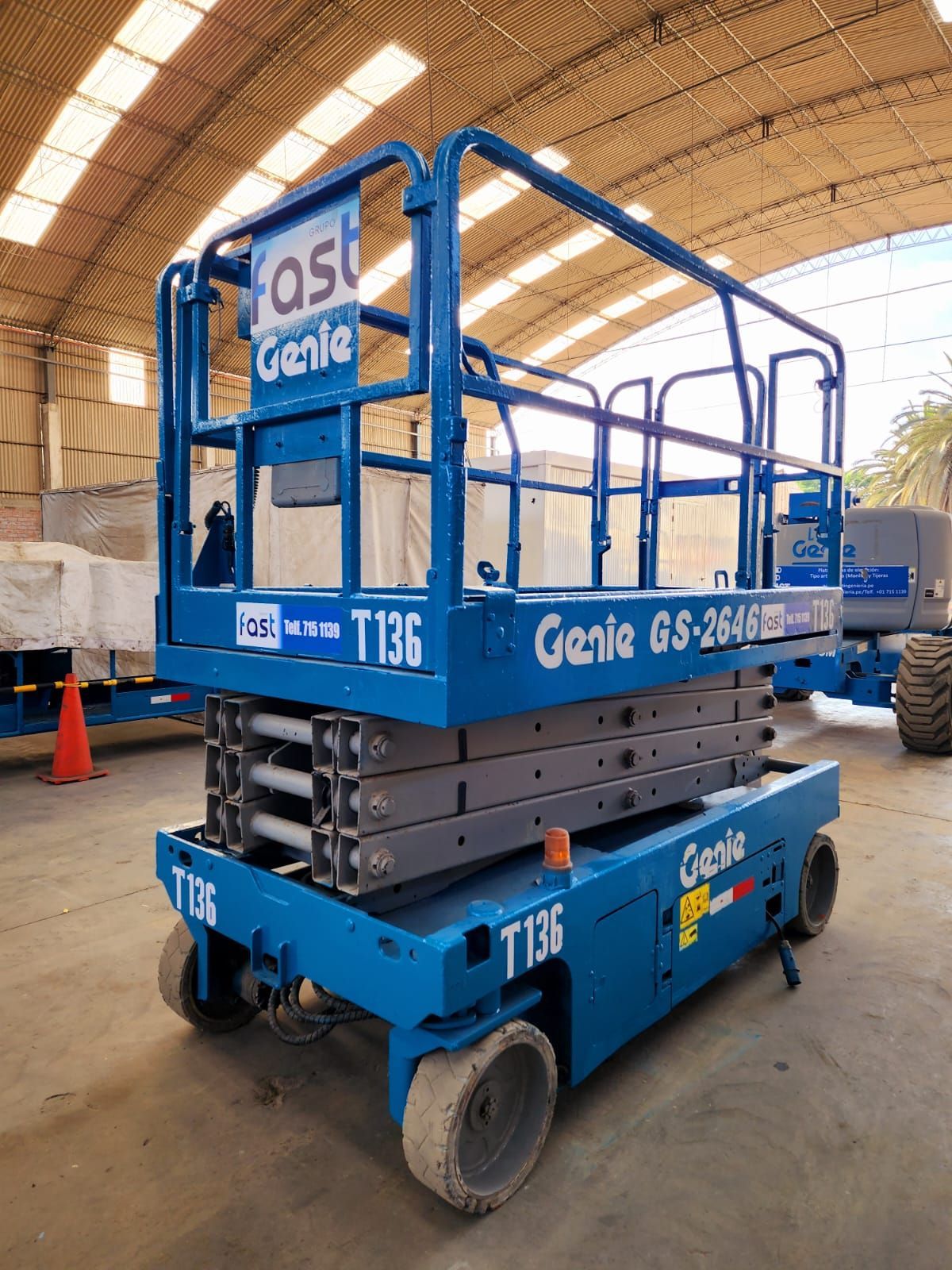 Plataforma elevadora de tijera Blue Genie en un almacén, con plataforma elevada y barandillas de seguridad.