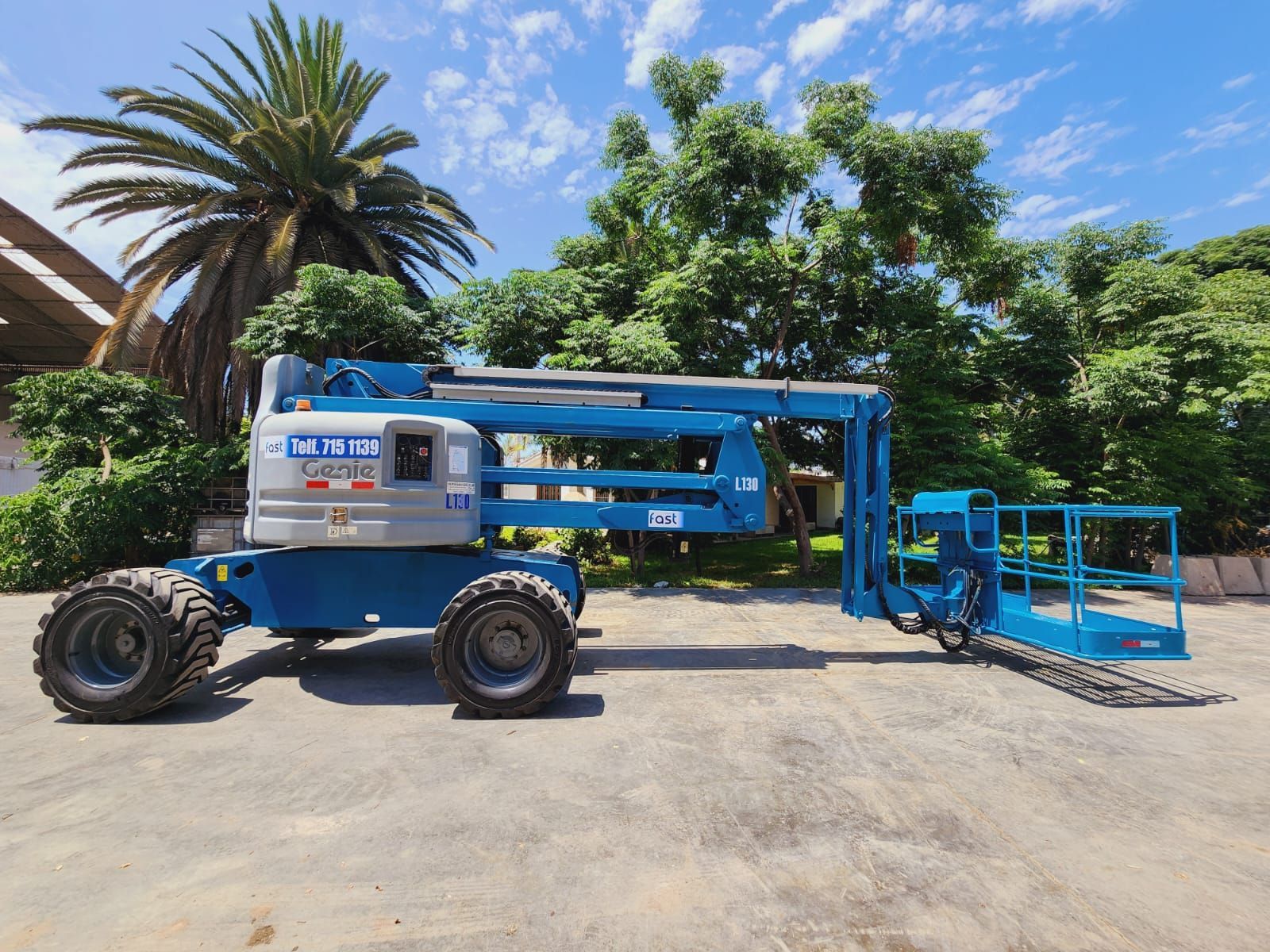 Una plataforma elevadora Blue Genie estacionada al aire libre cerca de palmeras bajo un cielo despejado.