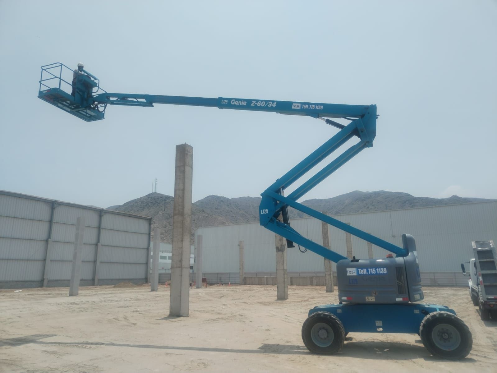 Una plataforma elevadora azul se extendía sobre una polvorienta obra en construcción, cerca de muros de hormigón y un pilar.