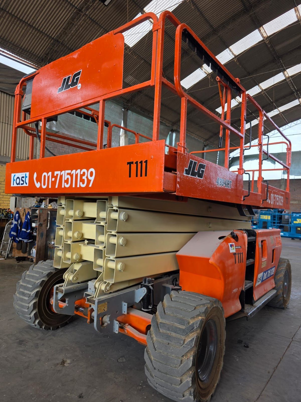 Trabajadores con cascos de seguridad ensamblan una plataforma elevadora de tijera amarilla en un taller de almacén.