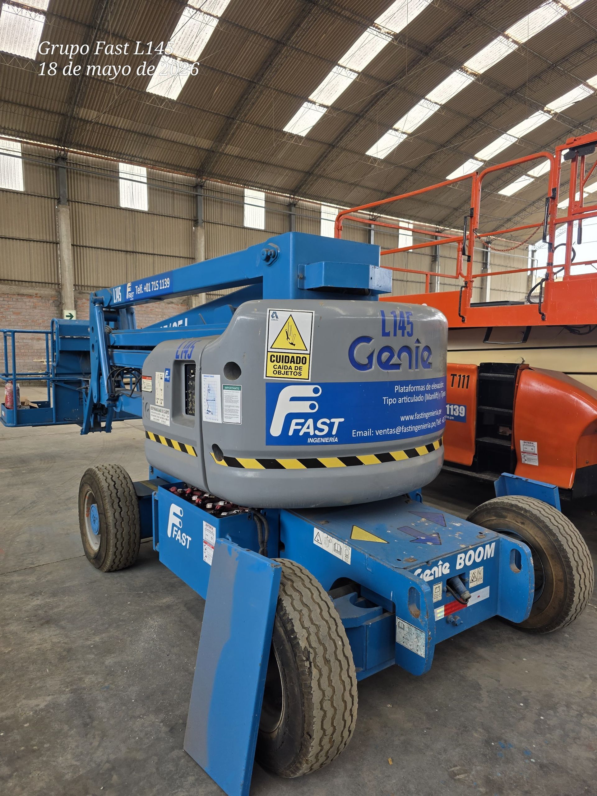 Plataforma elevadora de tijera Blue Genie Lift en un almacén, con ruedas grandes y brazos de plataforma elevados.