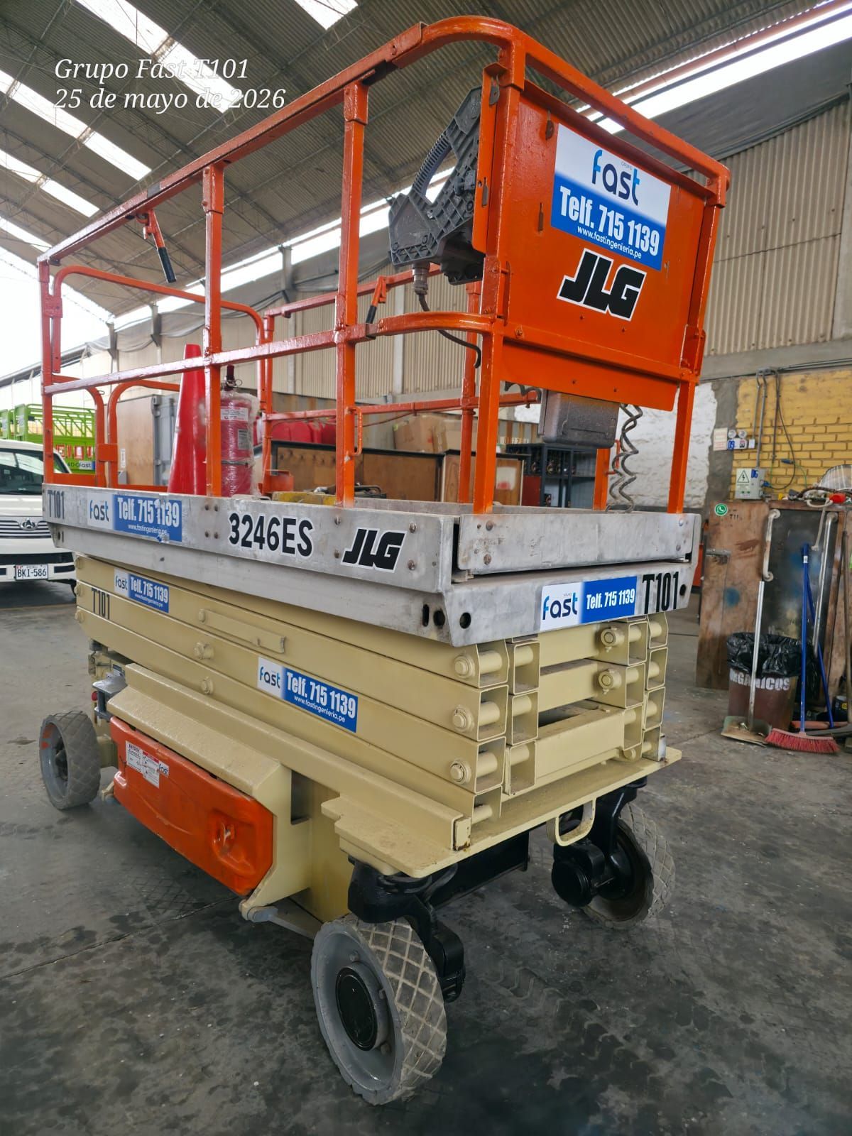 Plataforma elevadora de tijera naranja y beige sobre ruedas en un taller de almacén.