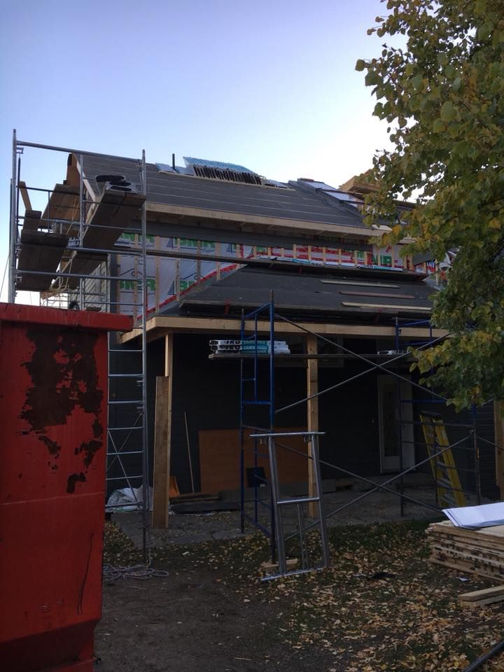 Une benne rouge se trouve devant une maison en construction.