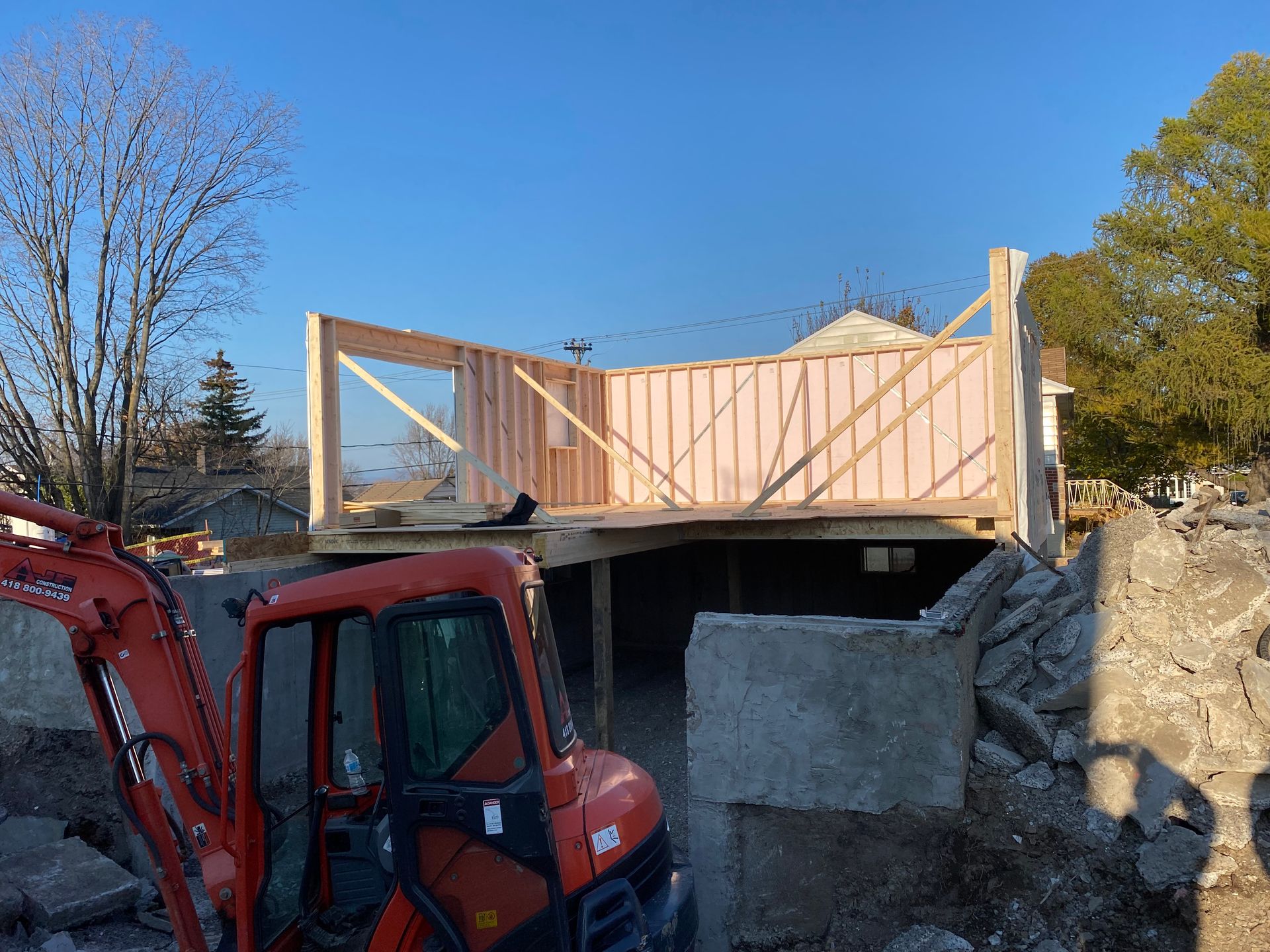 Une excavatrice rouge est garée devant une maison en construction.