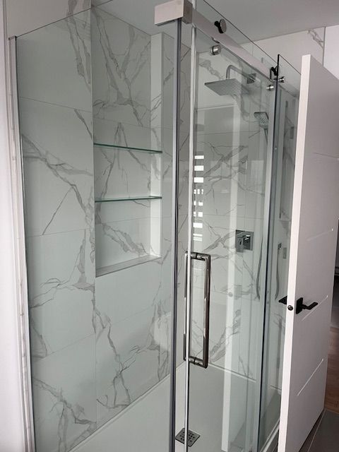 Une cabine de douche avec portes coulissantes en verre et murs en marbre.
