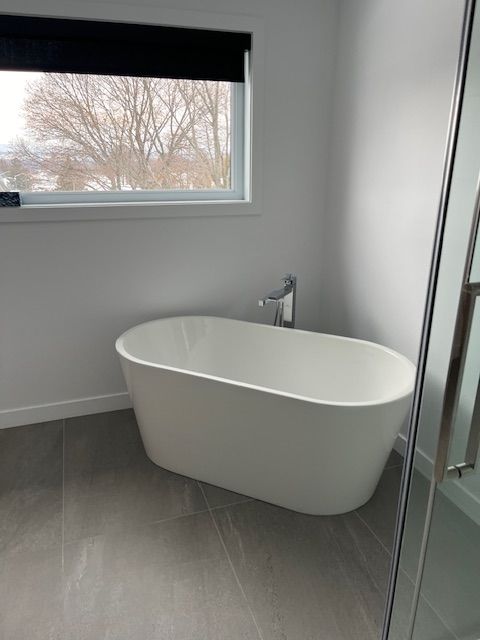 Une baignoire blanche se trouve dans une salle de bain à côté d'une fenêtre.