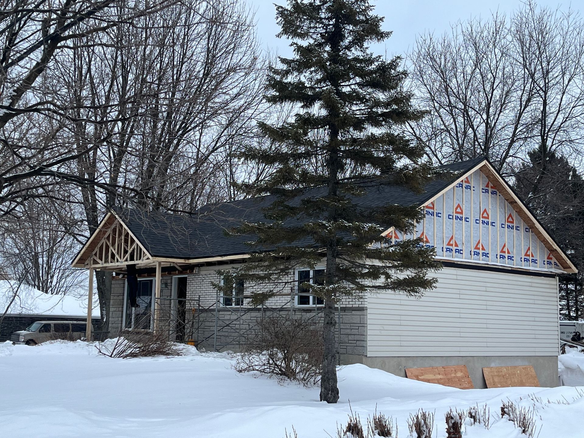 Une maison en construction sous la neige avec un arbre au premier plan.