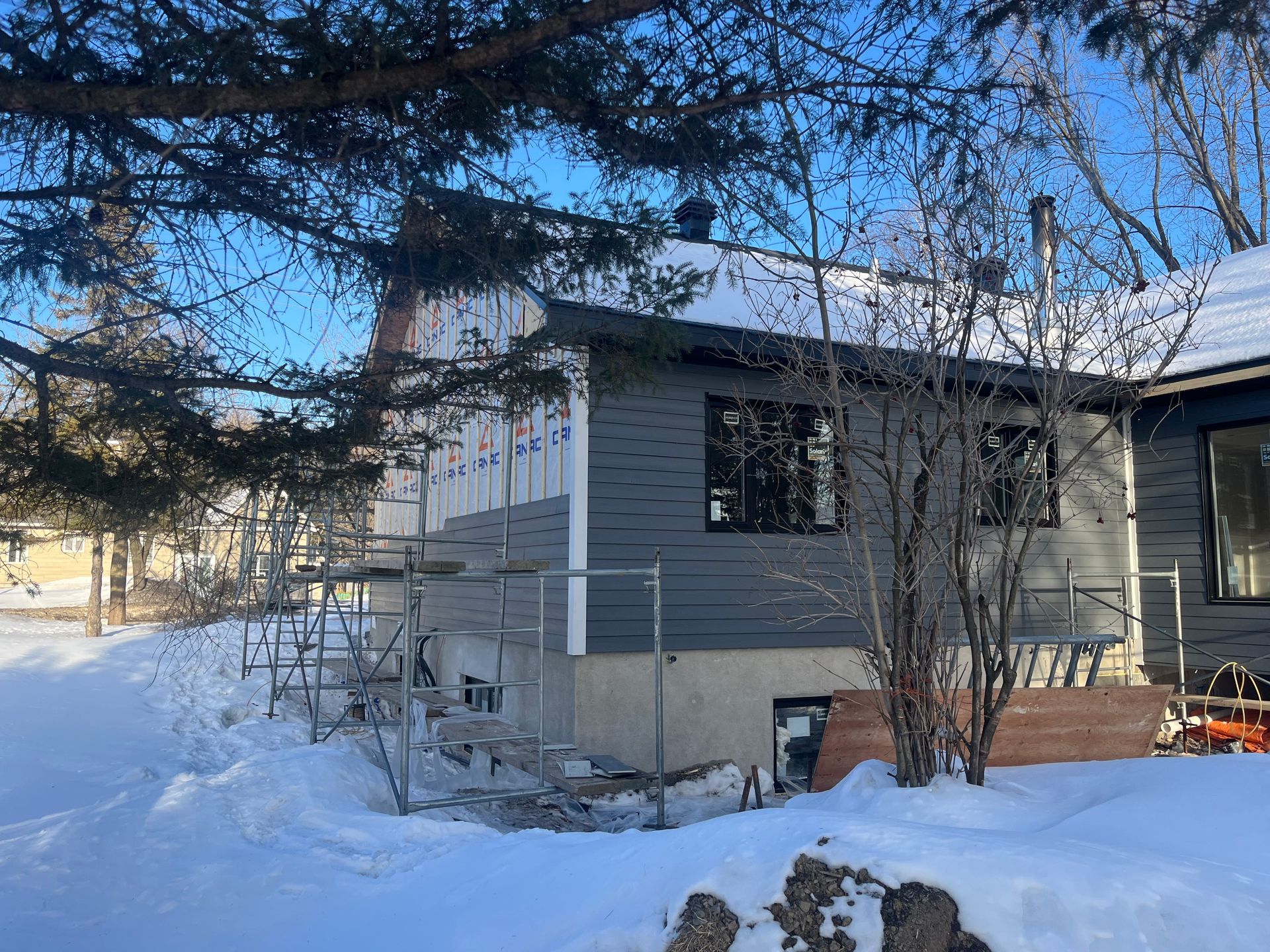 Une maison est en construction dans la neige à côté d'un arbre.
