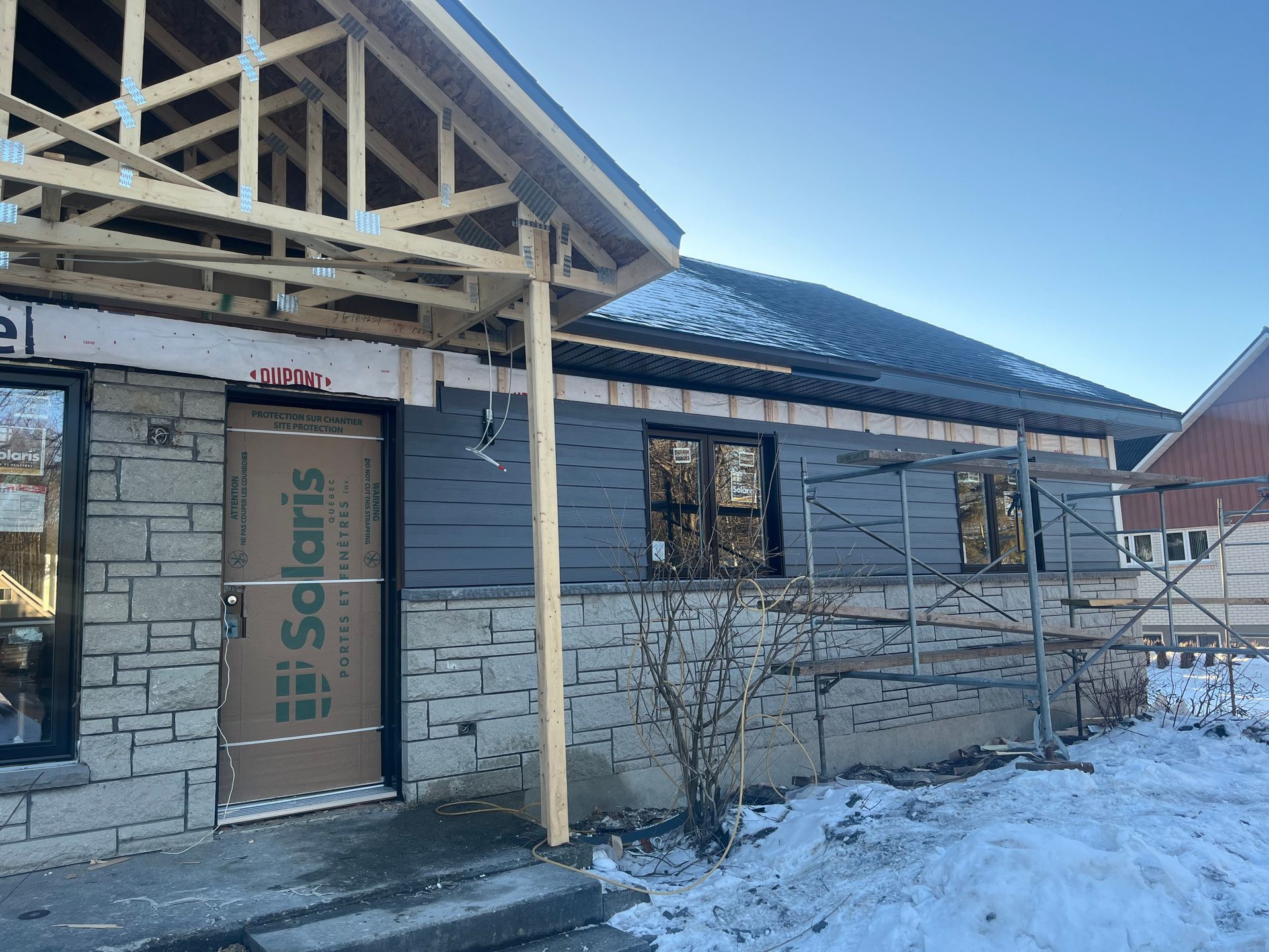 Une maison est en construction dans la neige avec un toit en bois.