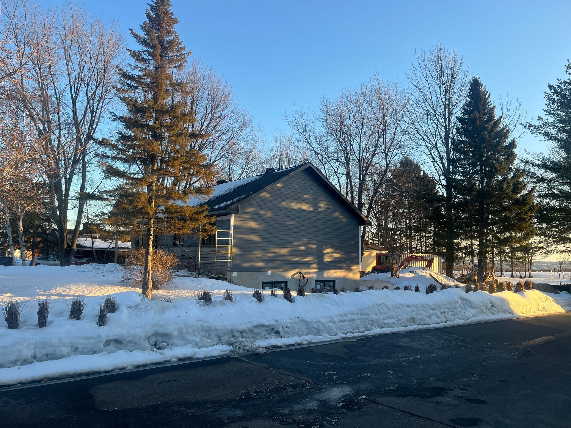 Une maison est entourée de neige et d'arbres par une journée ensoleillée.
