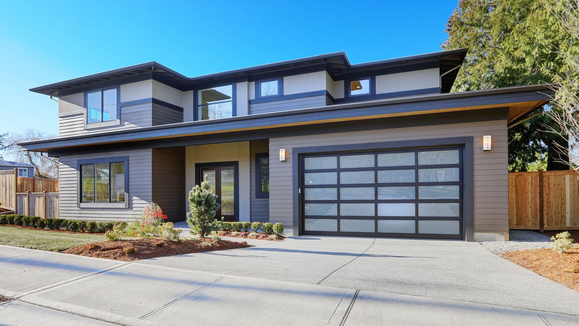 Une maison moderne avec une grande porte de garage et une allée en béton.