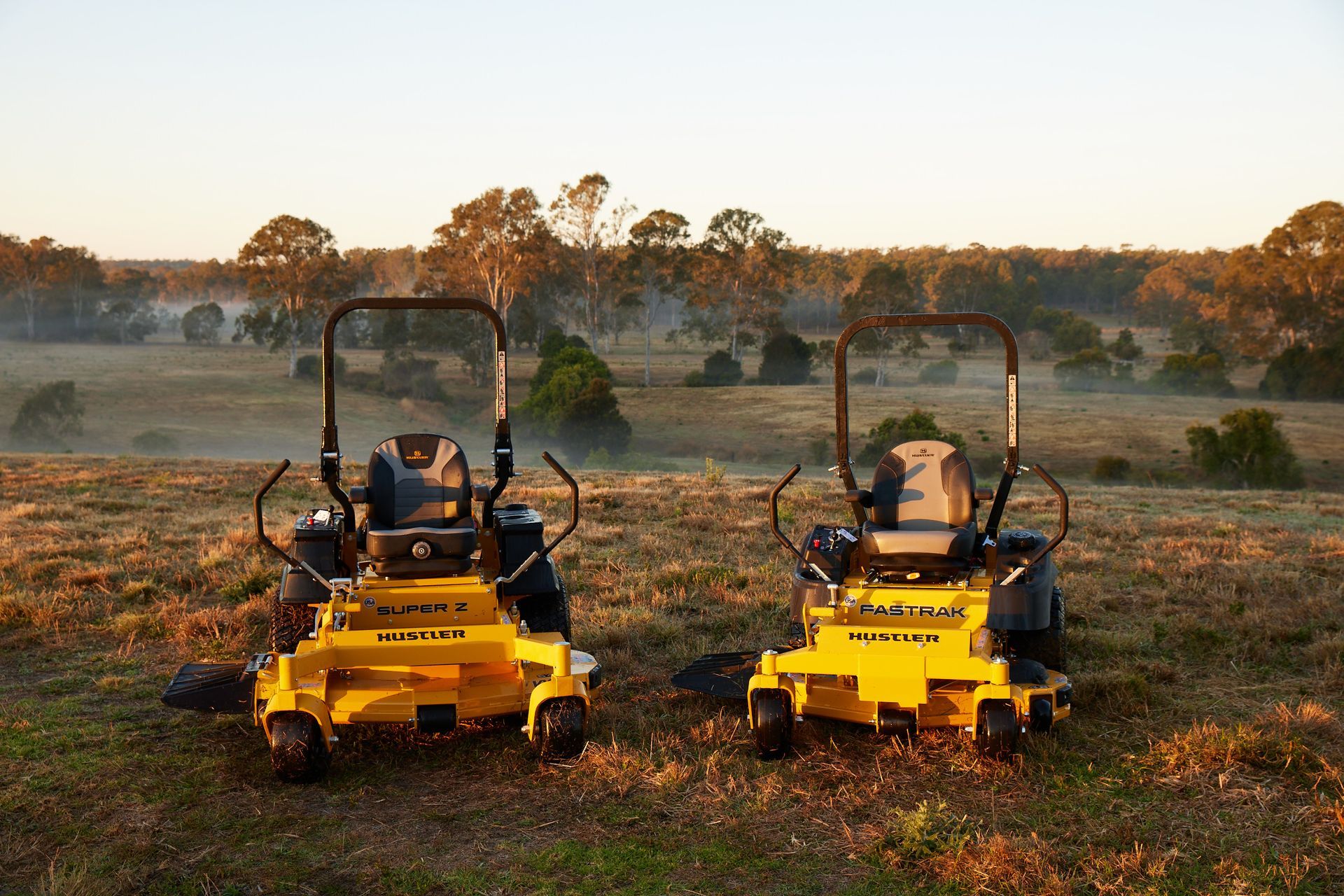 two hustler ride on mowers in front of orange bright sunset and bush land