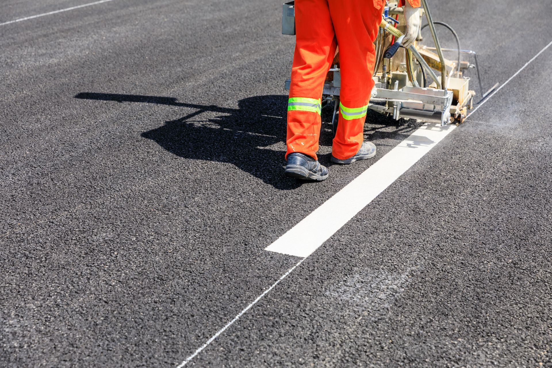A man in orange pants is painting a white line on the road.