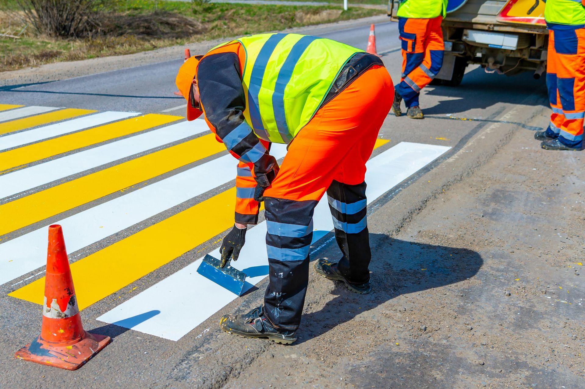 A man is painting a crosswalk on the side of the road.