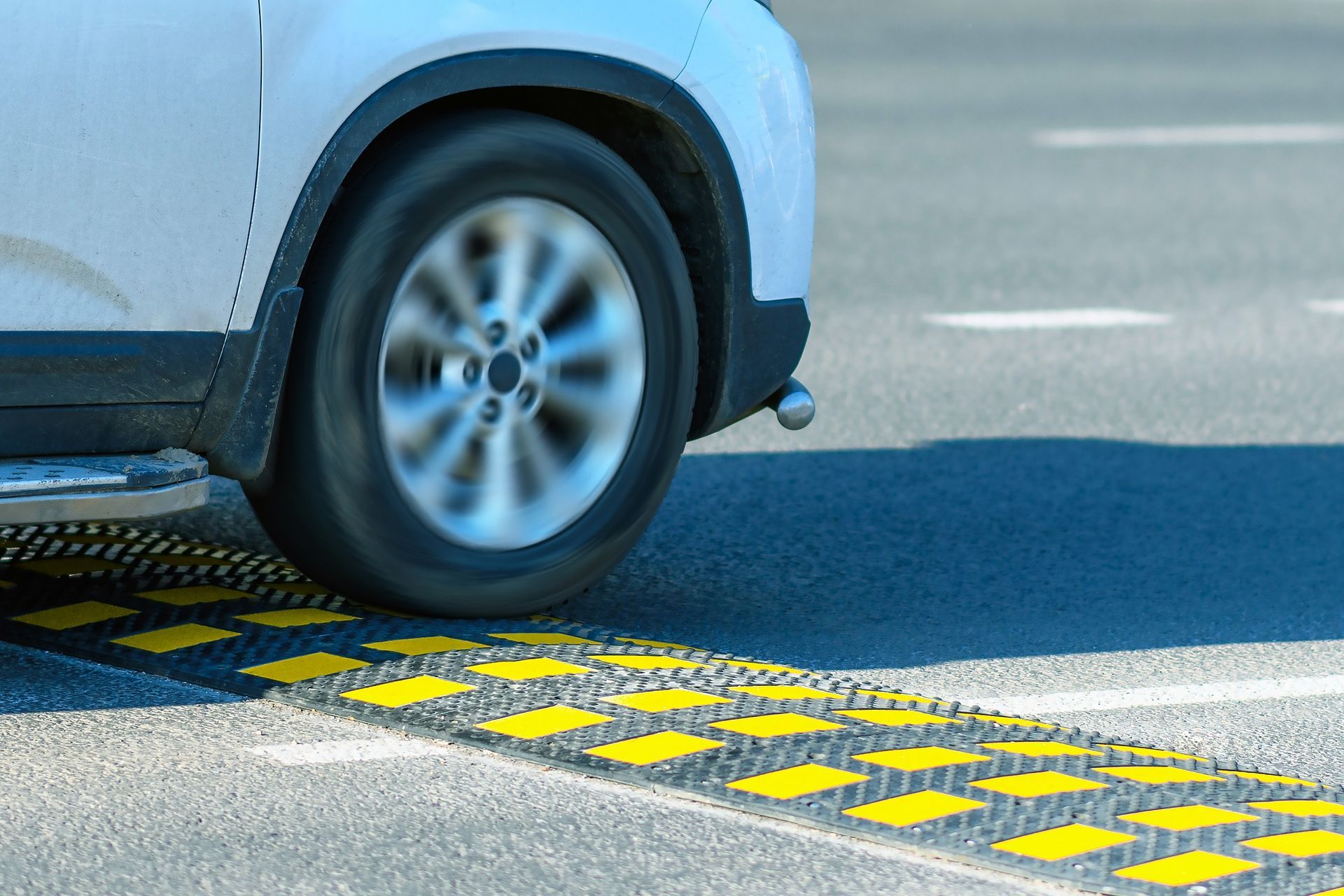 A white car is driving down a road with a speed bump.
