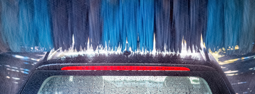 A car undergoing an automatic wash, with blue rotating brushes cleaning the rear windshield