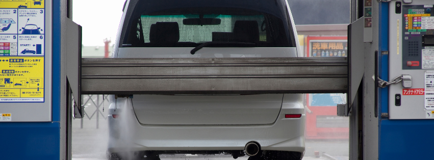 A white car undergoing an automated wash inside a modern car wash station, with control panels