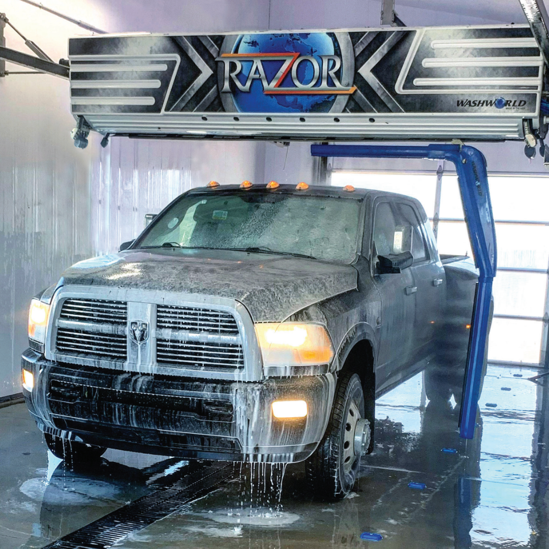 The image shows a large truck inside an automatic car wash, with foam and water flowing down the vehicle's surface.