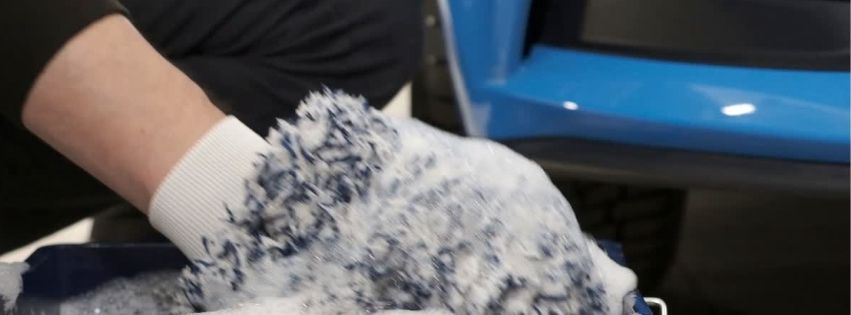 a person cleaning a car, likely using a wash mitt and soap
