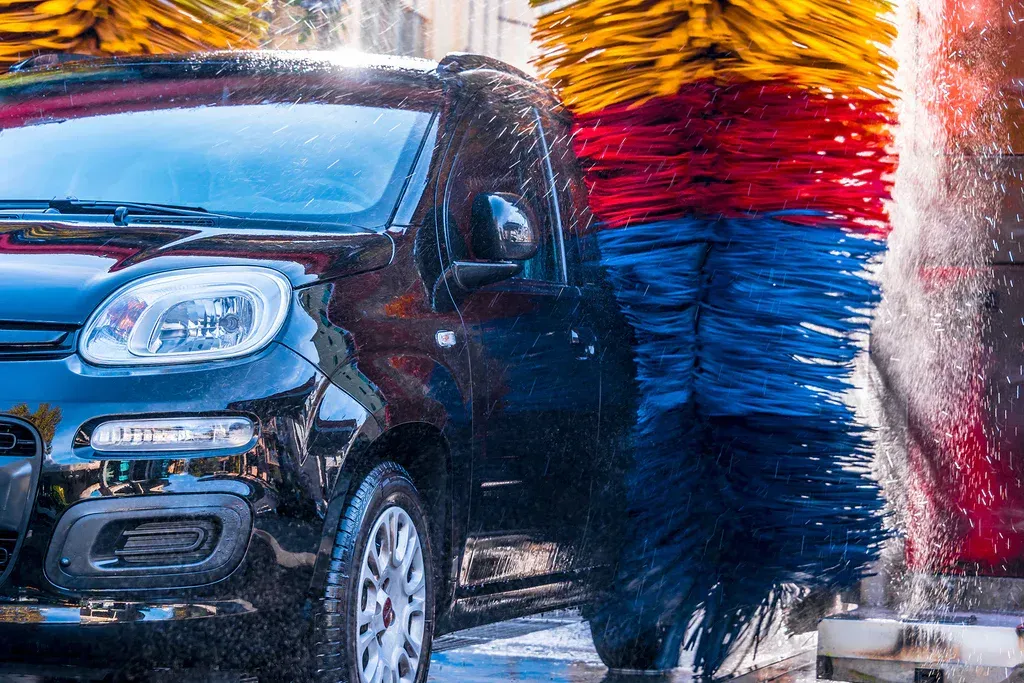 Black car being cleaned by red, yellow, and blue rotating brushes in an automatic car wash.