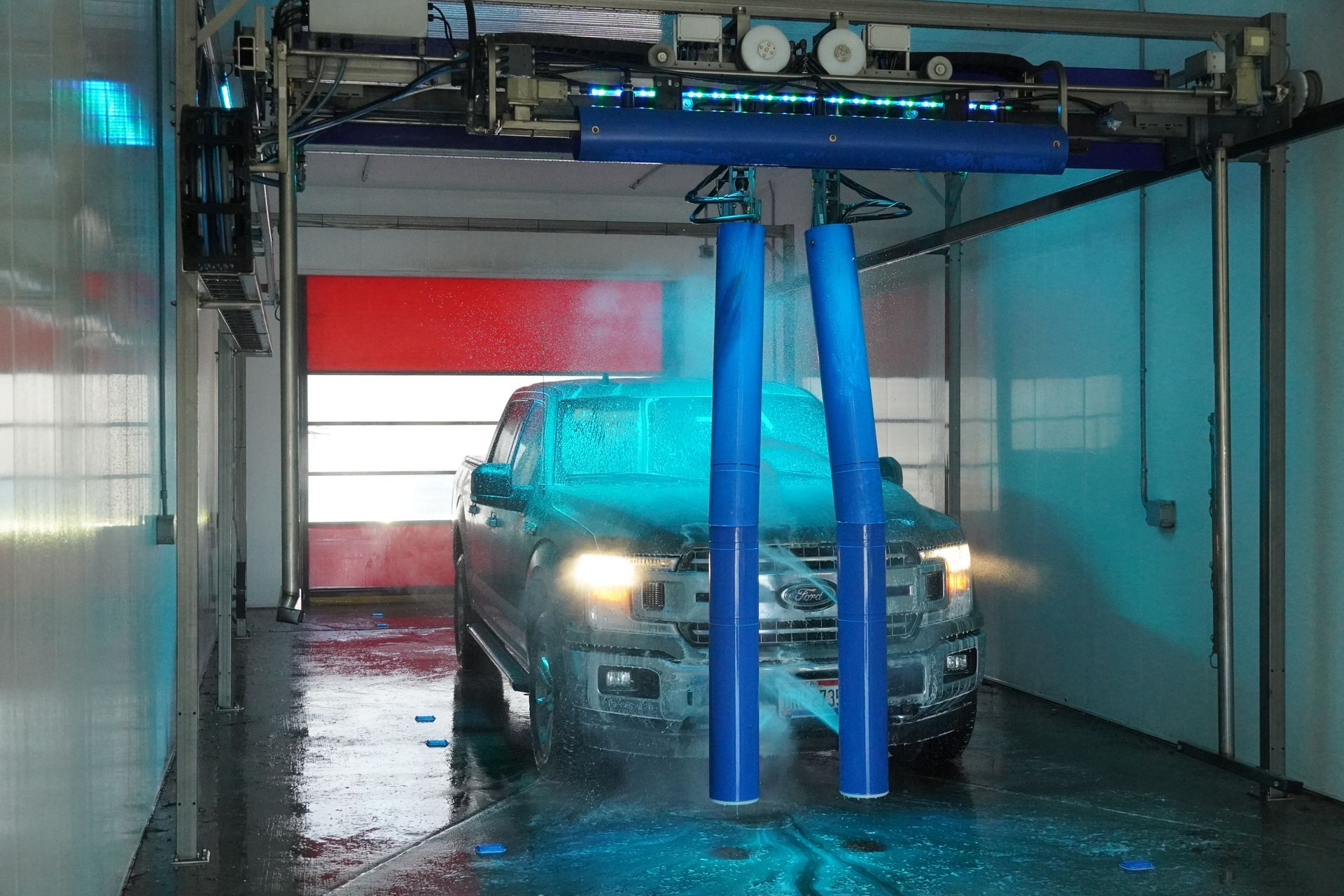 Pickup truck going through an automated car wash with blue spray nozzles.