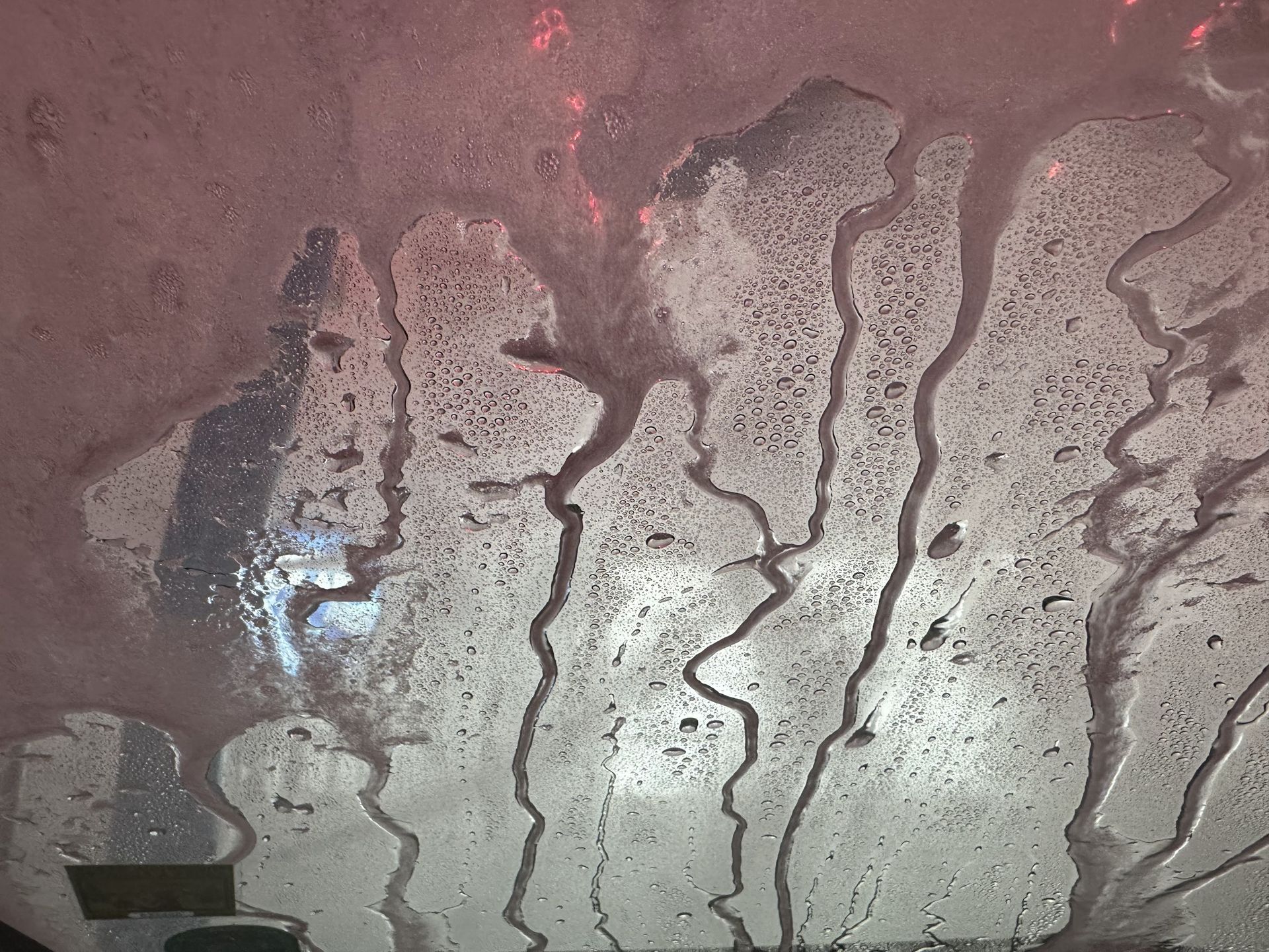 Soapy water and foam dripping across a car windshield during a wash.