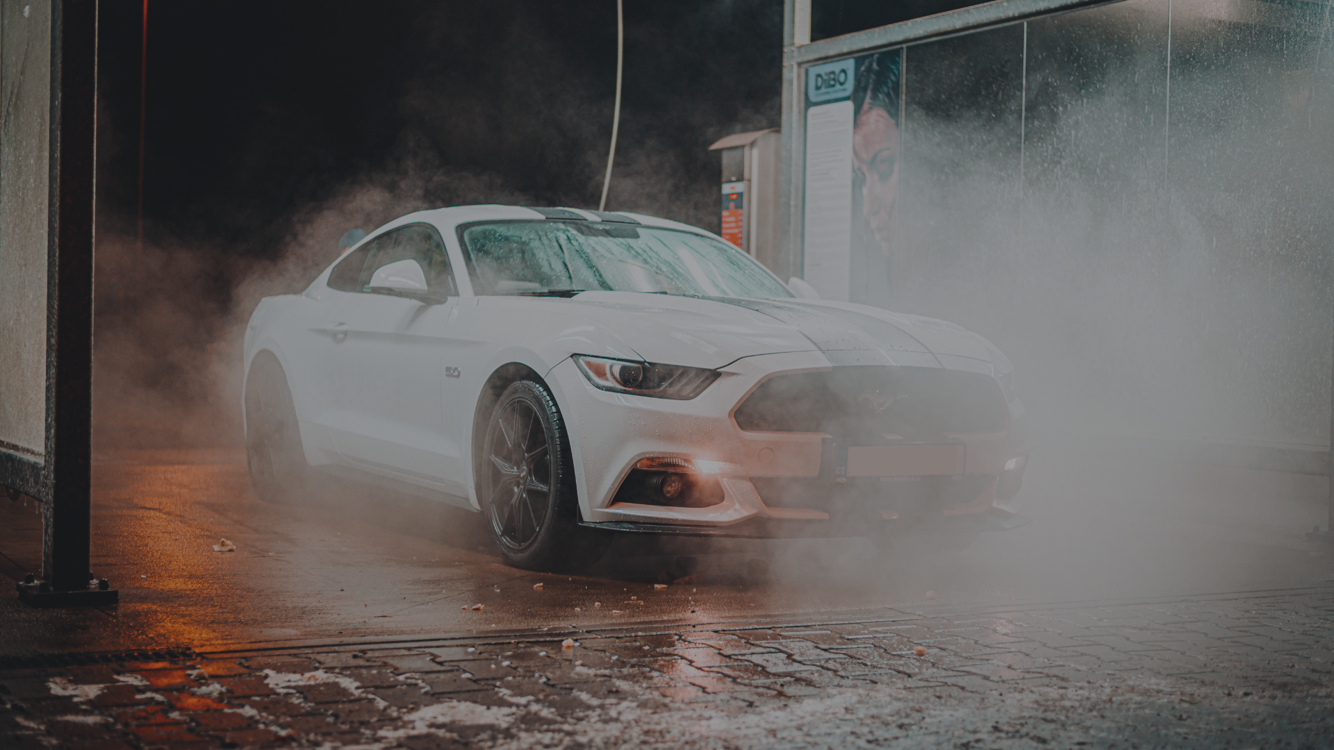 The image shows a white sports car, likely a Ford Mustang, being washed at a car wash.