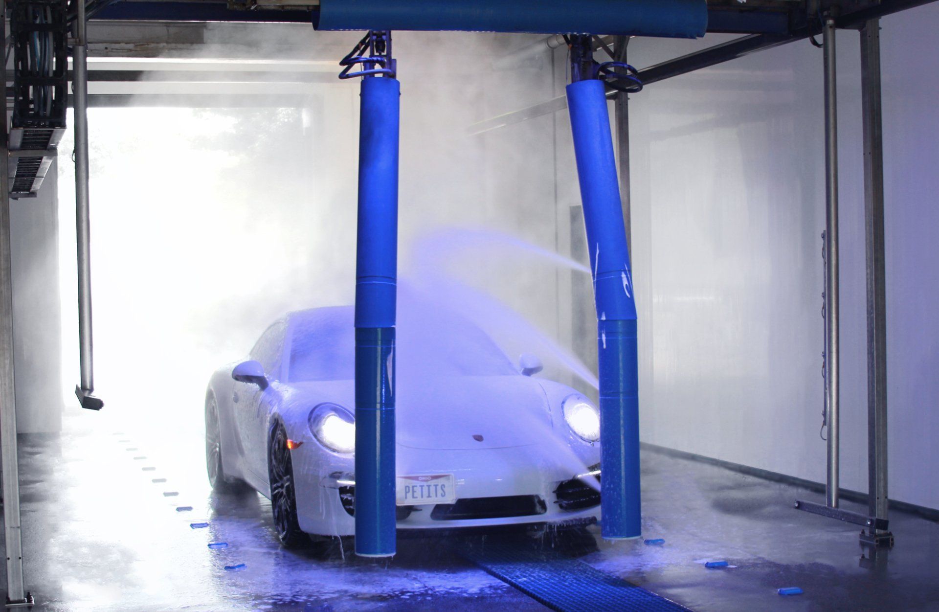 White sports car being washed in an automatic car wash with blue high-pressure sprayers.