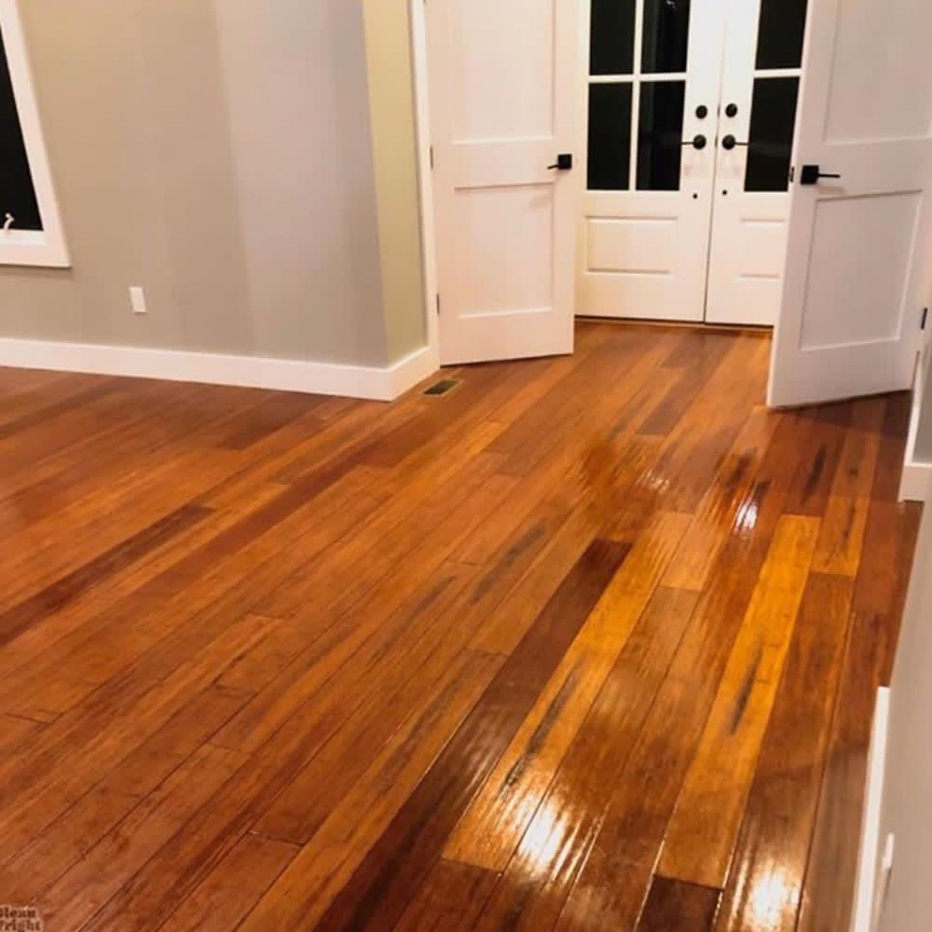 Glossy hardwood floors in a bright empty room with white French doors open to a hallway.
