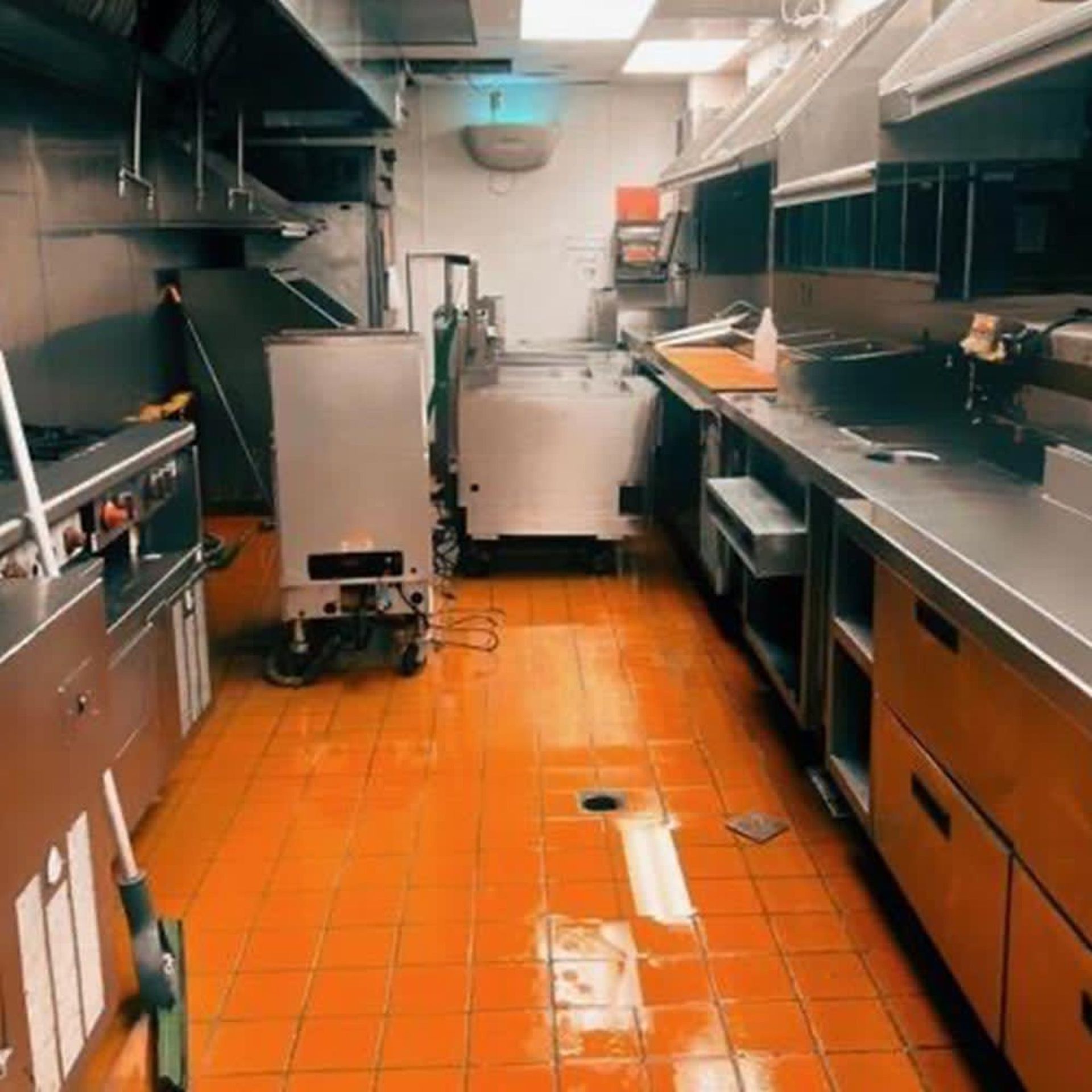 Empty commercial kitchen with stainless steel counters and orange tile floor