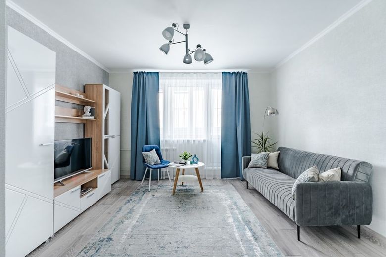 Bright living room with gray sofa, blue curtains, TV unit, and a small coffee table on a light rug.