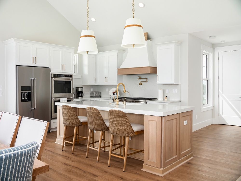 Bright modern kitchen with white cabinets, stainless appliances, and a wooden island with wicker bar stools