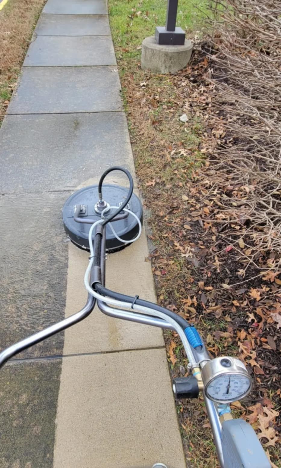 A machine is cleaning a sidewalk with a pressure gauge attached to it.