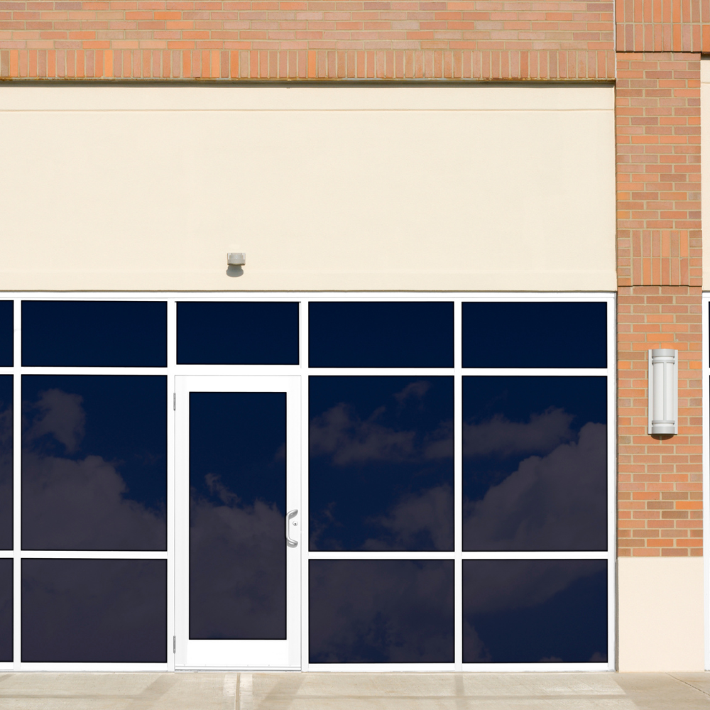 Exterior of a commercial building with dark windows and a white door, red brick and beige walls.