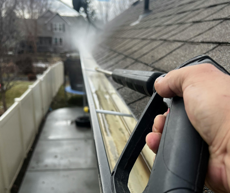 Person using a pressure washer to clean a gutter on a house.