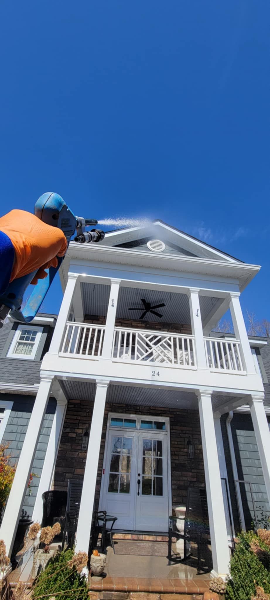 A man is cleaning the roof of a house with a pressure washer.