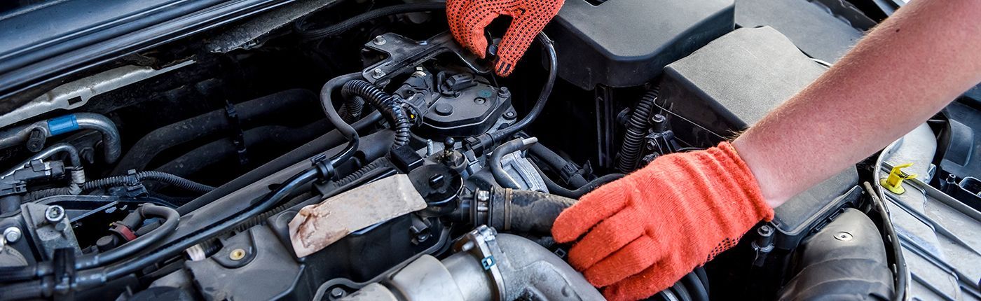 Mechanic in orange gloves working on car engine, inspecting parts.