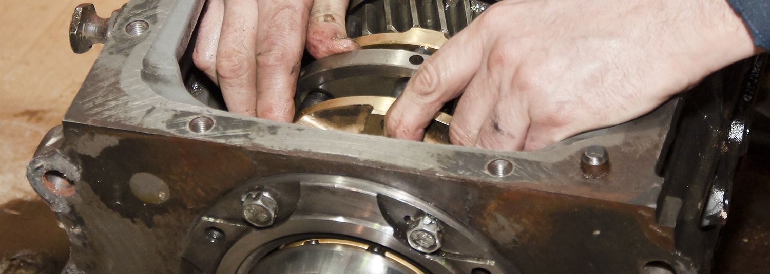 Hands working on a gear mechanism inside a metal housing.