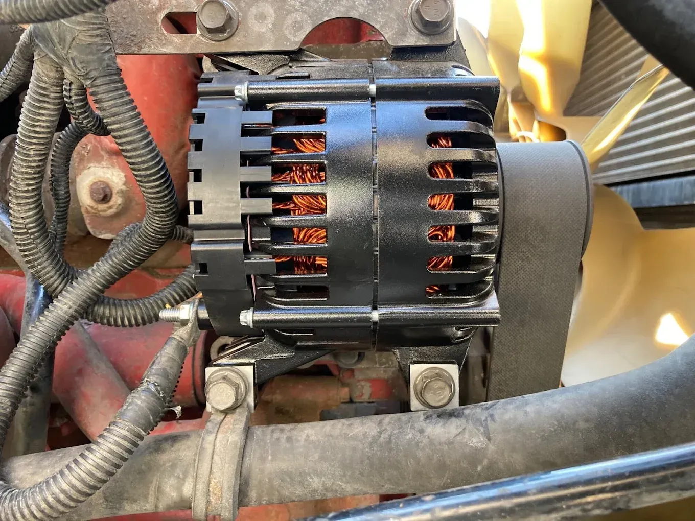 A black alternator is sitting under the hood of a car.