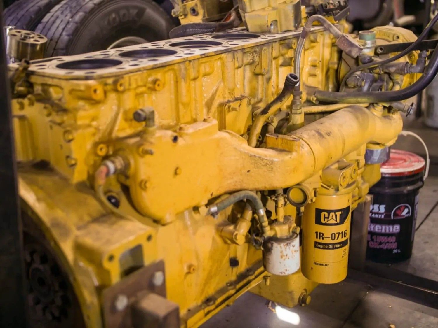 A yellow cat engine is sitting next to a bucket of oil.